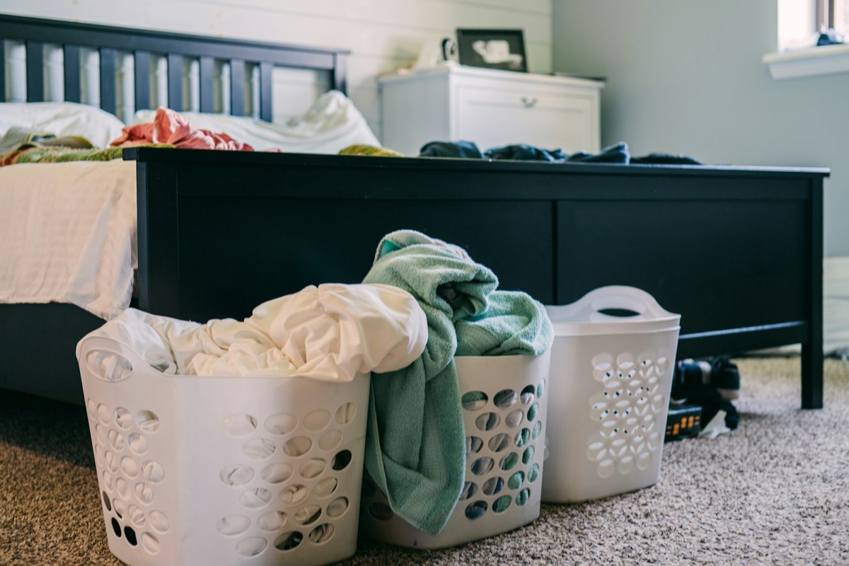 Trois paniers de linge pleins au pied d’un lit, en fin de journée.