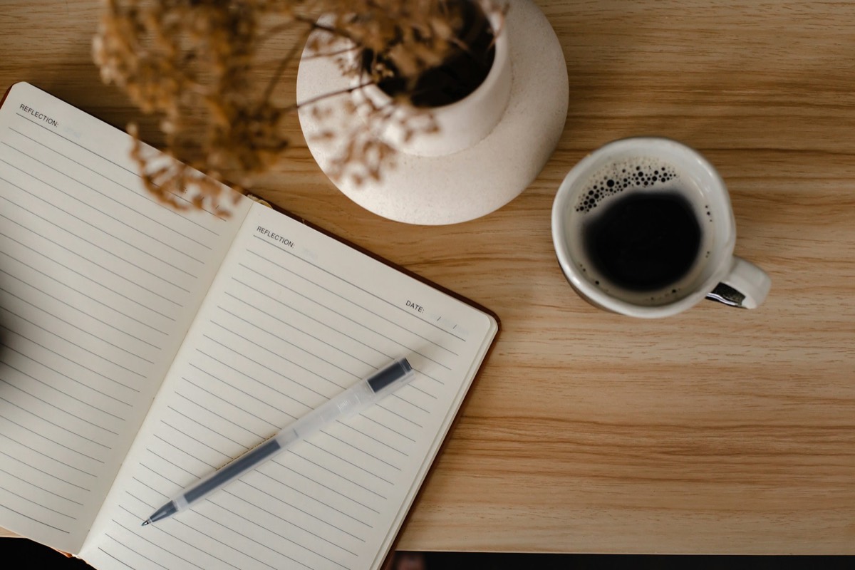 Un carnet ouvert, un stylo et une tasse de café sur une table en bois.